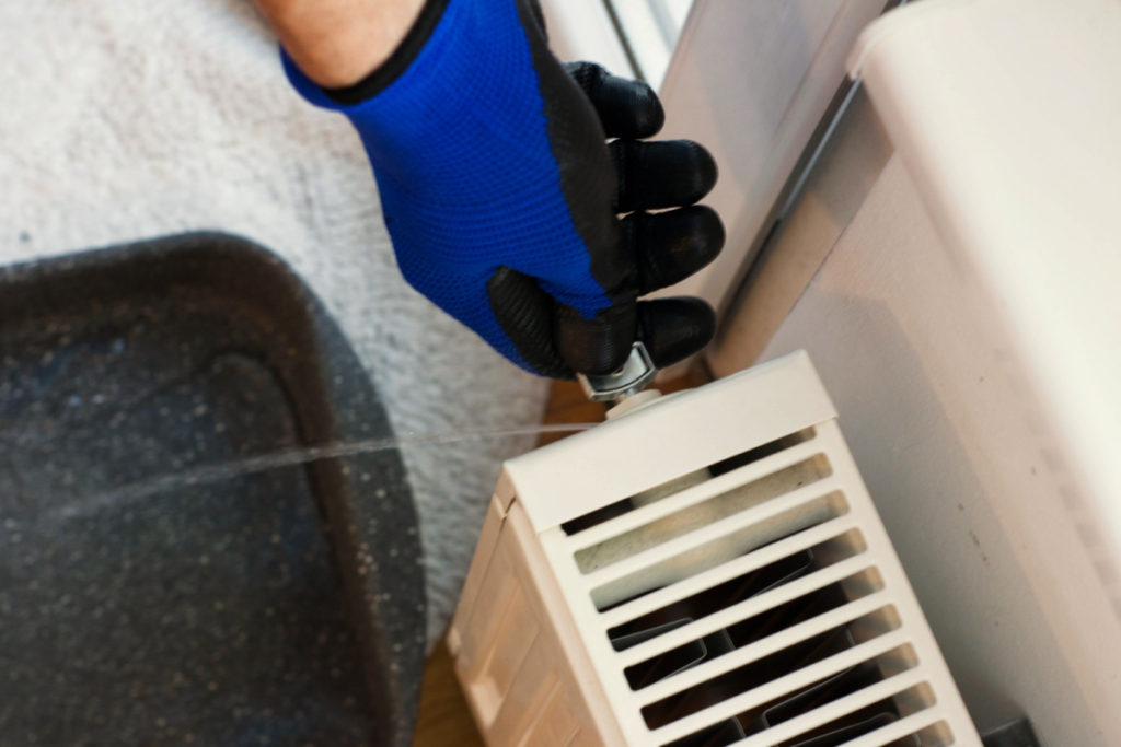 image showing a hand in a blue glove using a radiator key to bleed out water