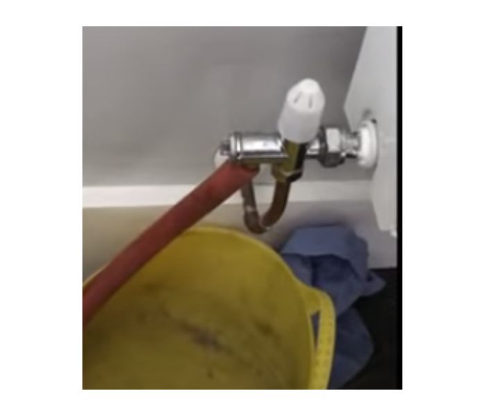 image showing a flexible hose connected to a radiator drain valve with a yellow bucket underneath to catch seeping water